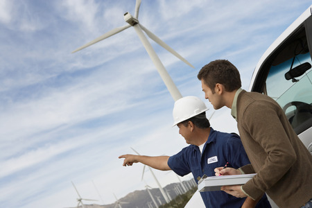 Engineers examining wind turbines by car at wind farmの写真素材