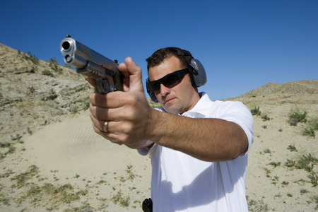 Man aiming hand gun at firing range in desert