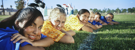 Teenage girls (13-16) lying in row on soccer field