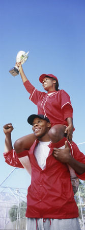 Woman holding trophy, sitting on man's shoulders, low angle viewの写真素材