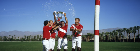 Polo team celebrating with trophy on fieldの写真素材