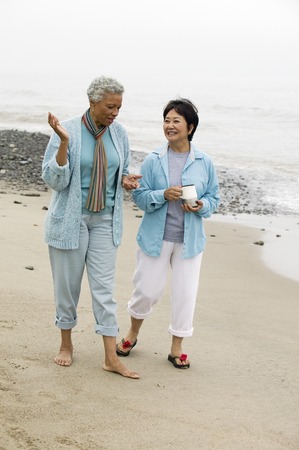 Two middle-aged women talking on beachの写真素材