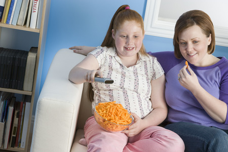 Overweight girl and mother watching television on sofaの写真素材