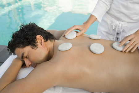 Man having stone therapy by swimming poolの写真素材