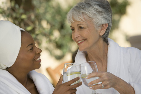 Two women in bathrobes, toasting drinksの写真素材