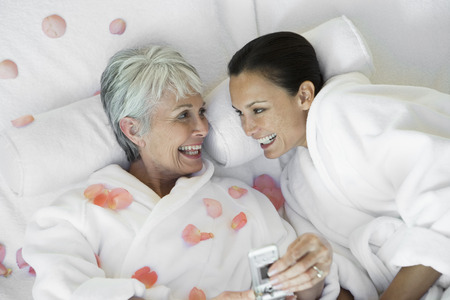 Mother and daughter with mobile phone on bedの写真素材