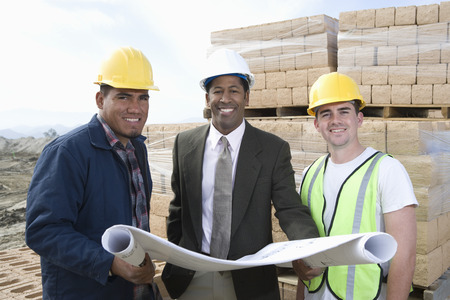 Three construction workers standing on construction site with blueprints