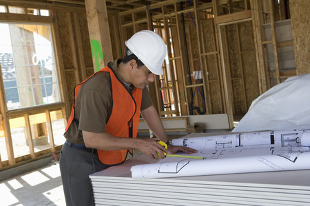 Construction worker using tape measure inside half constructed house