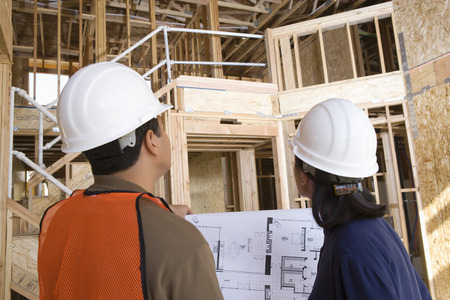 Architect and construction worker looking up while holding with blueprints inside half constructed houseの写真素材