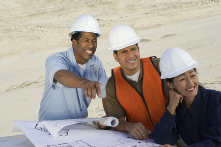 Architect and two construction workers looking at blueprints on construction site