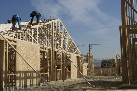 Two construction workers working on roof of half constructed house