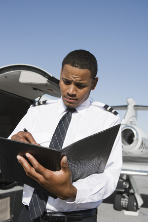 Airline pilot standing and making notes in front of airplane.の写真素材
