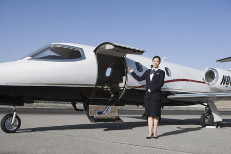 Female flight attendant standing in front of private jet on runway.の写真素材