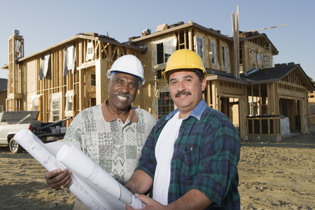 Two men holding blueprints at construction site, portraitの写真素材