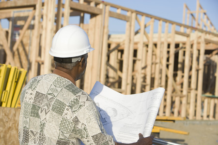 Middle-aged man with blueprints, construction site, back view