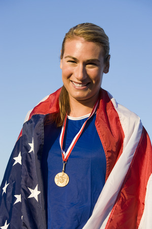 Female athlete wrapped in american flag with golden medal on neckの写真素材