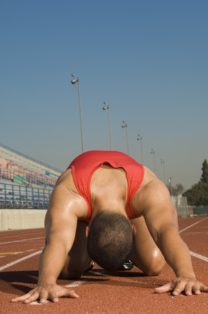 Male athlete stretching on trackの写真素材
