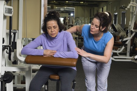 Trainer Assisting Senior Woman on Exercise Machineの写真素材