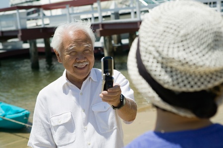 Senior man photographing wife using camera phone outdoorsの写真素材