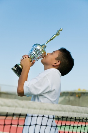 Young tennis player by net on court kissing trophy side viewの写真素材