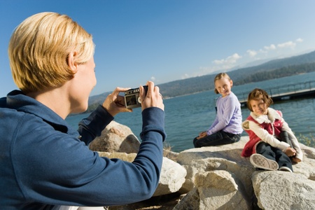Mother taking picture of daughters at the lakeの写真素材