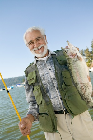 Middle-aged man holding up trout smiling (portrait)