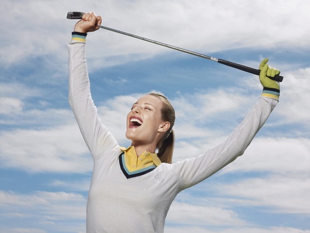Happy female golfer holding club against skyの写真素材