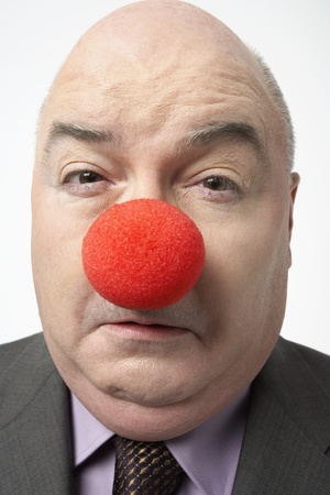 Bald businessman Wearing Clown Nose frowning close-upの写真素材