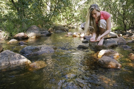 Teenage girl (16-17 years) squatting on stone by stream in forest