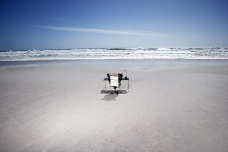 Senior business man sitting at office desk on beach elevated view back viewの写真素材