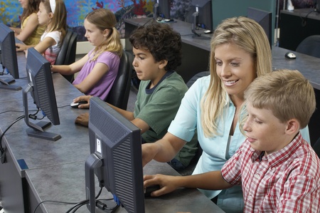 School children using computers with teacher in classroomの写真素材