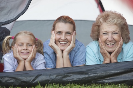 Mother daughter and grand-daughter lean on elbows smiling from tent