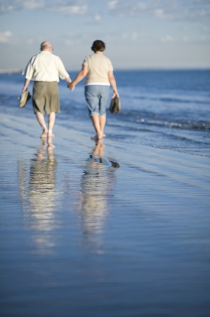 Senior couple walking on beach reflecting in waterの写真素材