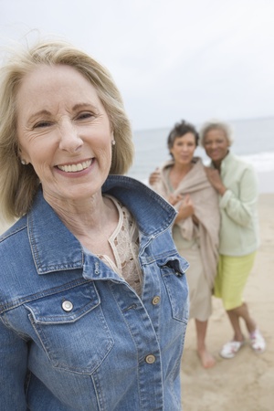 Mature woman in denim jacket on beach with her friendsの写真素材