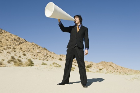 Businessman Using Megaphone in Desert