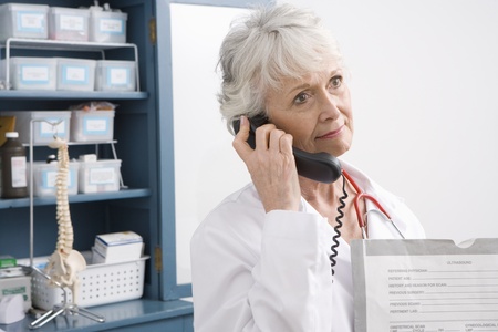 Senior medical practitioner stands on phone at medical cabinetの写真素材