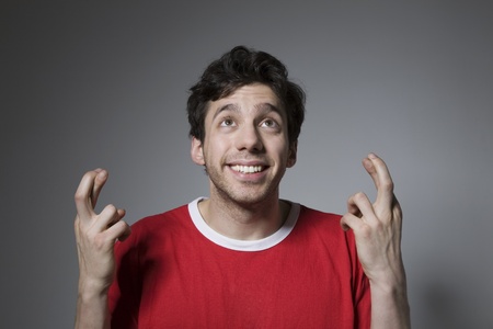 Young man in red top looking up with fingers crossed
