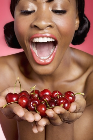 Cheerful young woman looking at cherry in her handsの写真素材