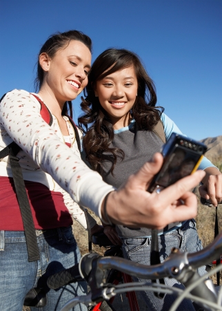 Two young women standing with bicycle photographing selves with digital camera.の写真素材