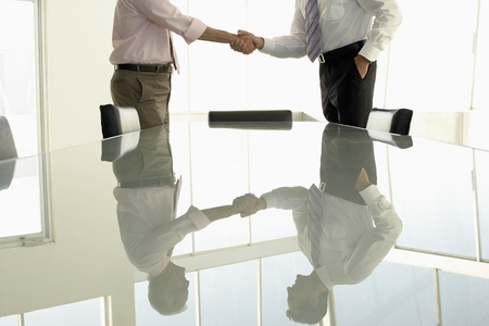 Businessmen shaking hands by conference table mid sectionの写真素材