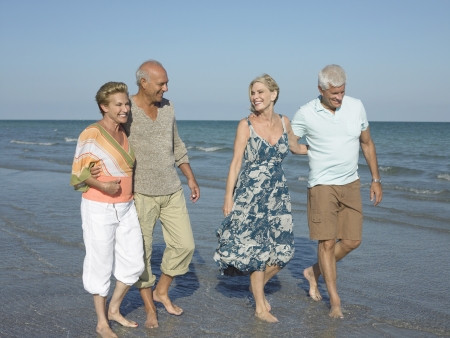 Two senior couples walking barefoot on beachの写真素材