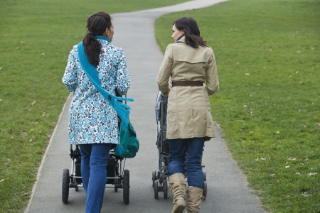 Back view of two mothers pushing strollers in park