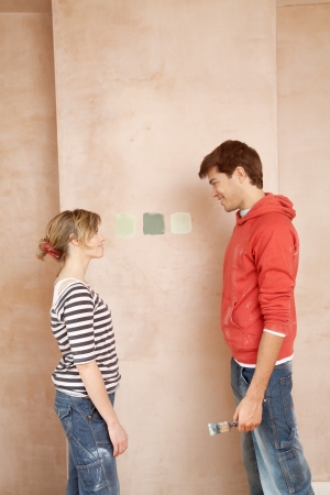 Couple standing face to face choosing paint colour samples on wallの写真素材