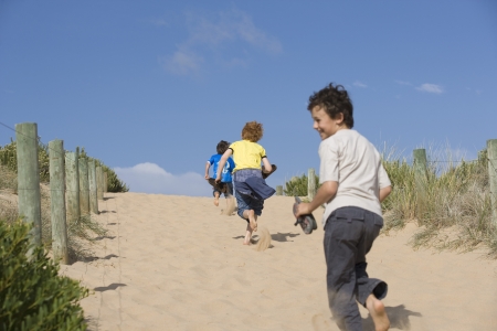 Three pre-teen boys running towards beachの写真素材