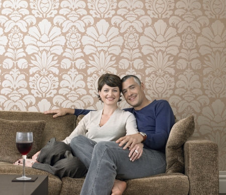 Smiling couple relaxing on sofa in living room (portrait)の写真素材