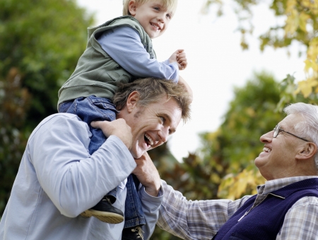 Boy (3-4) riding on father's shoulders grandfather looking on in yard low-angle view