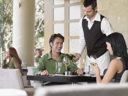 Waiter pouring wine for couple at outdoor restaurantの写真素材