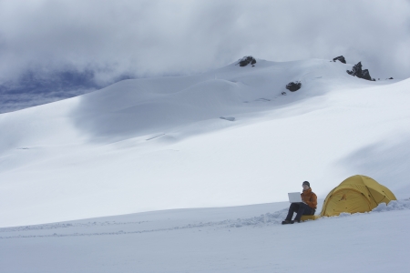 Hiker using laptop outside of tent on snowy mountain peakの写真素材