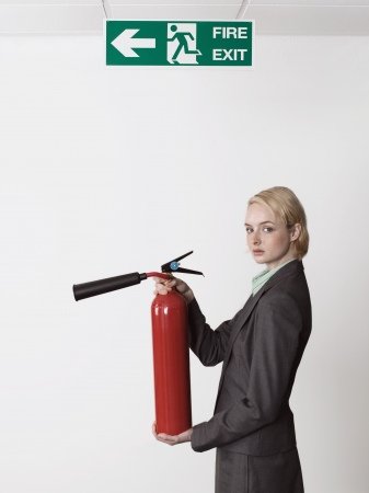 Businesswoman Holding Fire Extinguisher Under Exit Signの写真素材