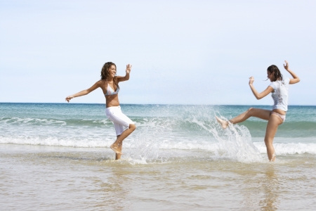 Two Young Women Splashing Each Other at Beachの写真素材